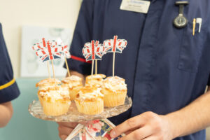 Person holding tray of cupcakes with crown-shaped flags and Union Jack flags