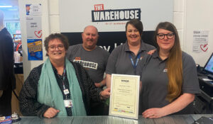 Three women and a man with framed certificate of Age Friendly Business Award at The Warehouse charity shop in Lincoln