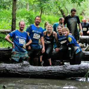 A group of 5 St Barnabas Supporters, wearing blue St Barnabas T-shirts, taking part in a wolf run tough Mudder challenge, within a forest.