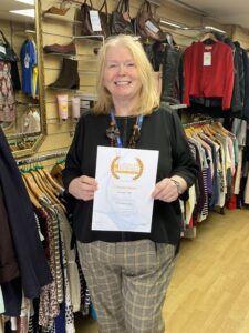 Woman with long blonde hair holding certificate in charity shop