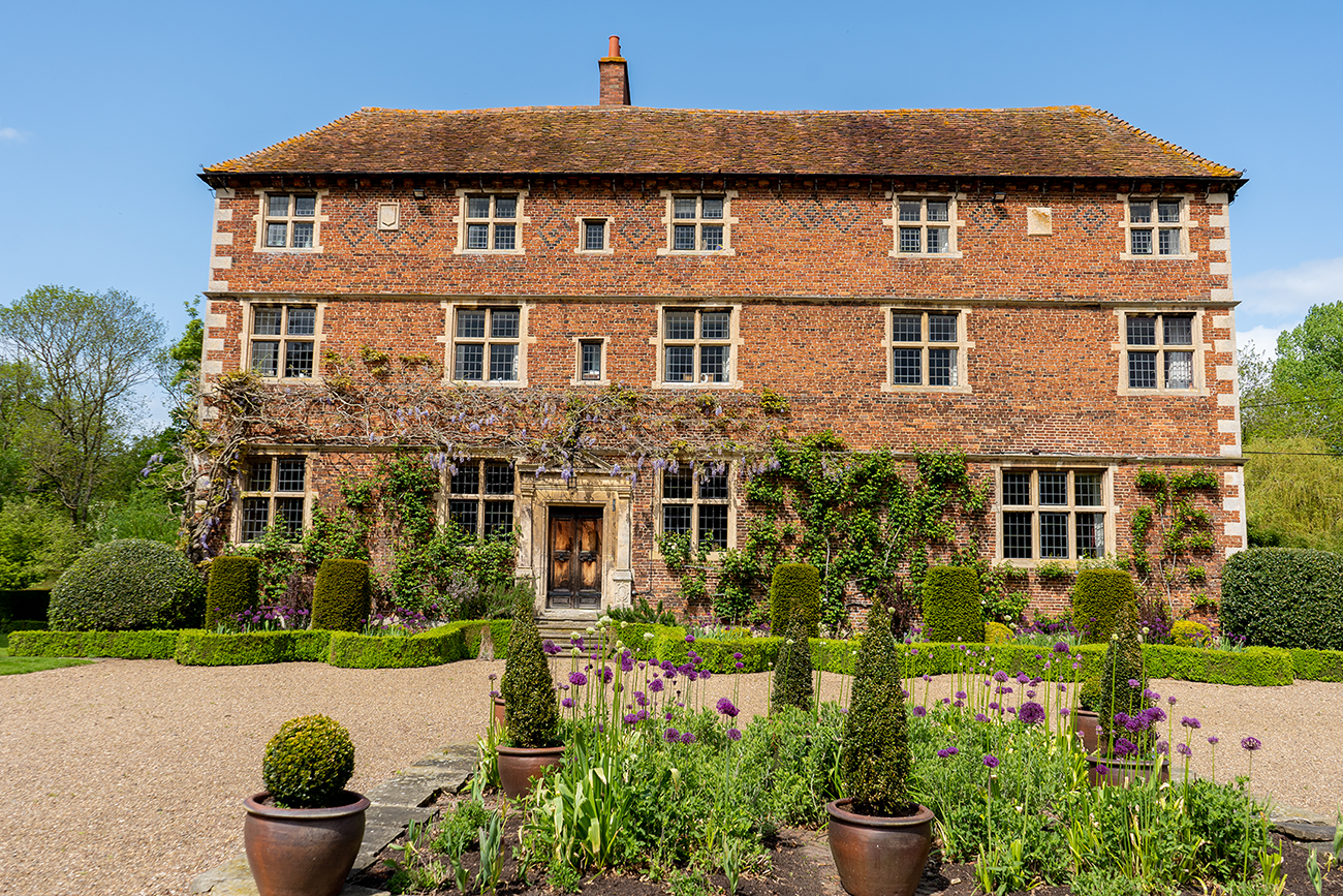 Aubourn Hall, a 17th century manor house with wisteria growing on the façade, winding shrubberies, potted and bedded plants.