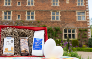 Red hamper with tea, cake and coffee, white heart sculpture against backdrop of a 17th manor house and gardens.