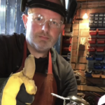 Brett Barker, one of the Artists for the St Barnabas HeART Trail. Man wearing safety goggles and gloves giving thumbs up inside a workshop environment.