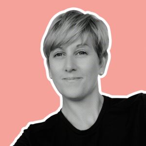 Pip Claffey, one of the Artists for the St Barnabas HeART Trail. Black and white photo of woman with short blonde hair and black top, against pink background.