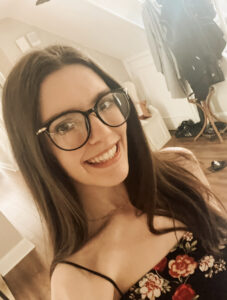 Rachel Benson, one of the Artists for the St Barnabas HeART Trail. Young woman with long brown hair and glasses, wearing floral top and smiling.