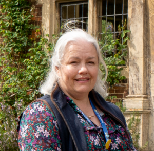Rebecca Franks, a white haired lady wearing floral top and blue St Barnabas lanyard, in outdoor setting.