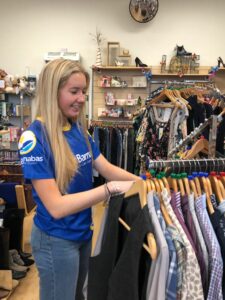 Young blonde woman wearing blue St Barnabas top at work in one of the charity shops