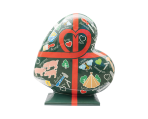 A Heart-shaped sculpture, painted with a green background, surrounded by illustrative renderings of equipment depicting the construction sector. This sculpture is part of the St Barnabas HeART Trail.