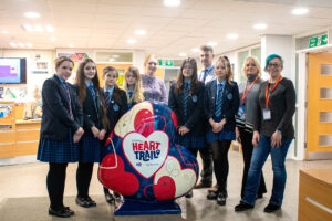 School children in uniform and several adults with large heart-shaped sculpture in red, white and blue.