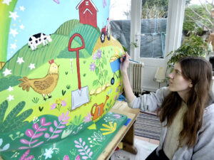 Brown haired young woman, artist Phillippa or Rachael Corcutt working on painting a brightly coloured heart-shaped sculpture as part of the St Barnabas HeART TRail.