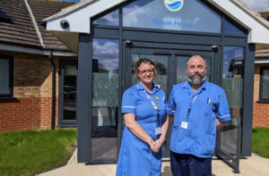 Woman and man in blue nurse uniforms in front of St Barnabas Wellbeing Centre, with large glass entry.