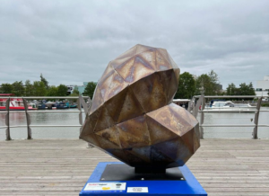 Metal heart-shaped sculpture on blue plinth by the Brayford in Lincoln, part of the St Barnabas HeART Trail