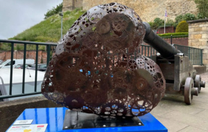 Metal heart-shaped sculpture in front of Lincoln Castle on blue plinth, part of the St Barnabas HeART Trail