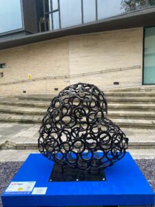 Heart-shaped sculpture made of horseshoes on blue plinth in front of steps of building, part of the St Barnabas HeART Trail