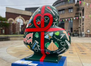 Heart-shaped sculpture painted green with red ribbon design and showing Lincolnshire towns and villages, part of the St Barnabas HeART Trail
