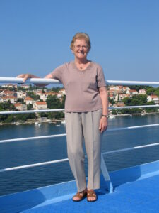 Elderly woman wearing soft colours on a boat with sea and sky in background.