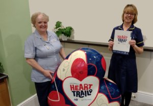 Two women wearing nurse uniforms with large heart-shaped sculpture in red, blue and white, part of the St Barnabas HeART Trail.