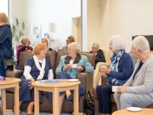 Group of elderly ladies sitting on chairs with wooden tables in front, at the St Barnabas Wellbeing Centre in Louth.