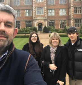 Selfie photograph of a man, a woman, a girl and boy by a stately manor.