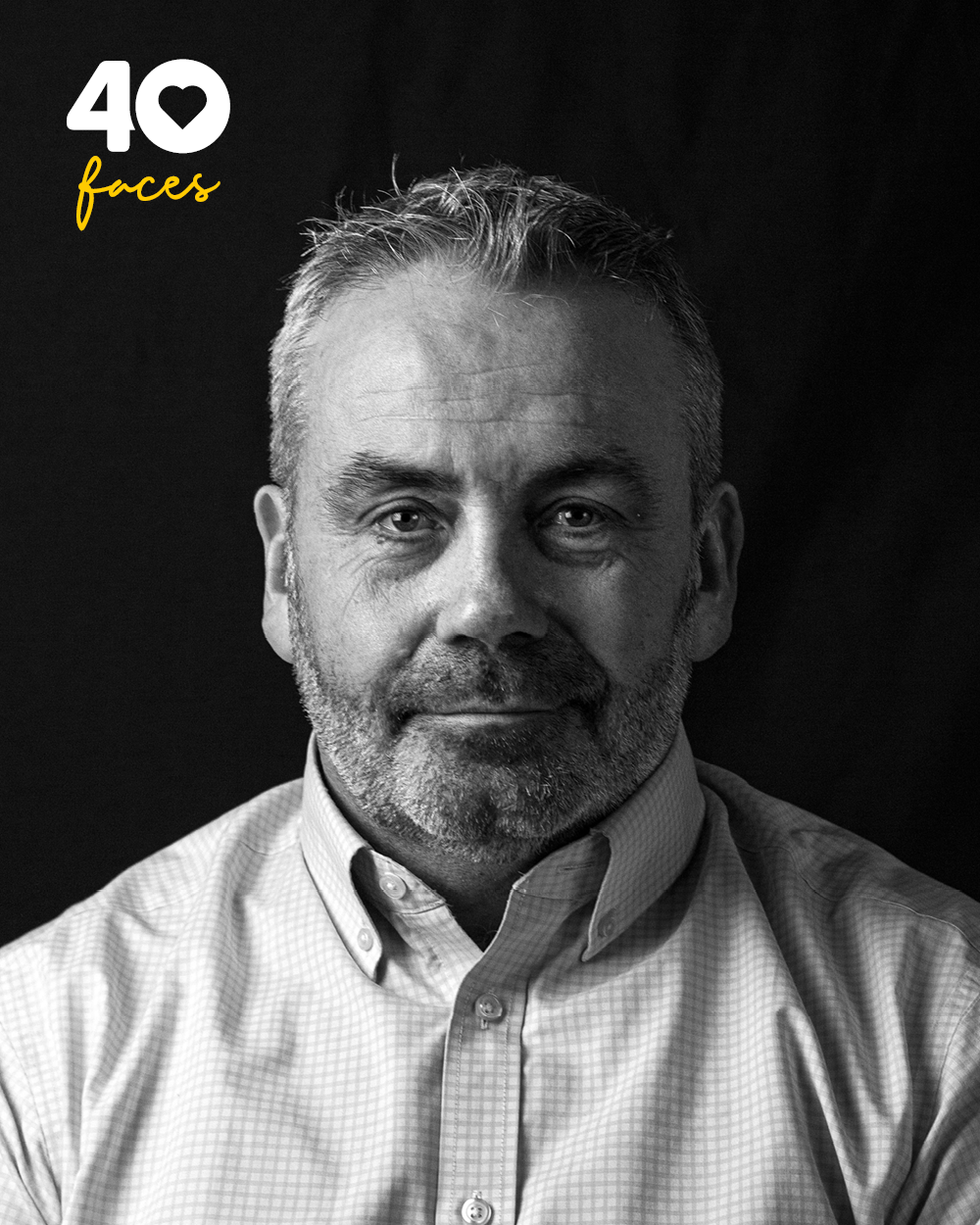 Black and white photograph of man with short hair and beard, wearing button-up shirt. On black background with logo in top left corner in white and yellow with text "40 Faces"