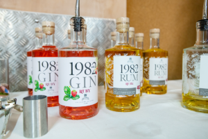 Several bottles of Est.1982 Ruby Gin and Rum on table with white table cloth, with steel shot measurer.