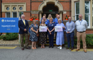 Group of people standing in front of the St Barnabas Inpatient Unit in Lincoln, holding signs with donation from Lincolnshire Co-op.