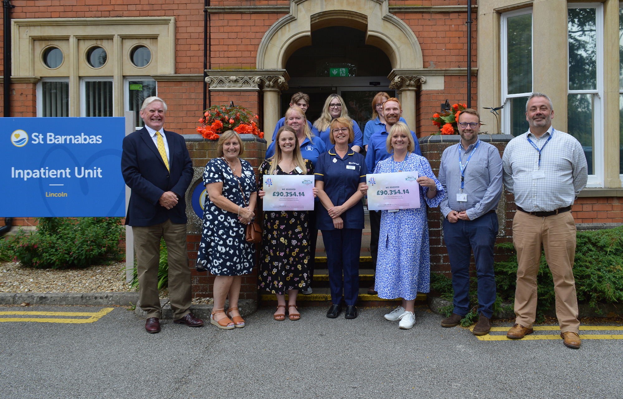 Group of people standing in front of the St Barnabas Inpatient Unit in Lincoln, holding signs with donation from Lincolnshire Co-op.