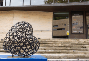 Sculpture made of horseshoes on blue plinth, outside of brick building with Lincoln Museum signage on door