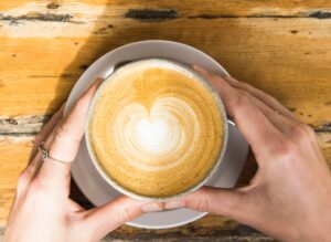 A cup of coffee, being held, on a wooden table.