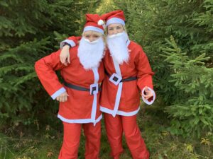 Two women dressed up in a Santa costume, stood within a forest.