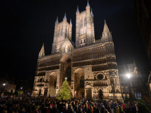 Lincoln Cathedral illuminated at night with St Barnabas Tree of Life and crowd of supporters