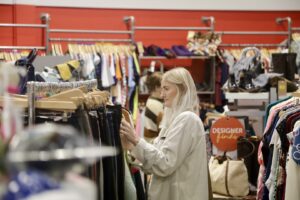 Blonde woman wearing a beige jacket browsing a clothing rail