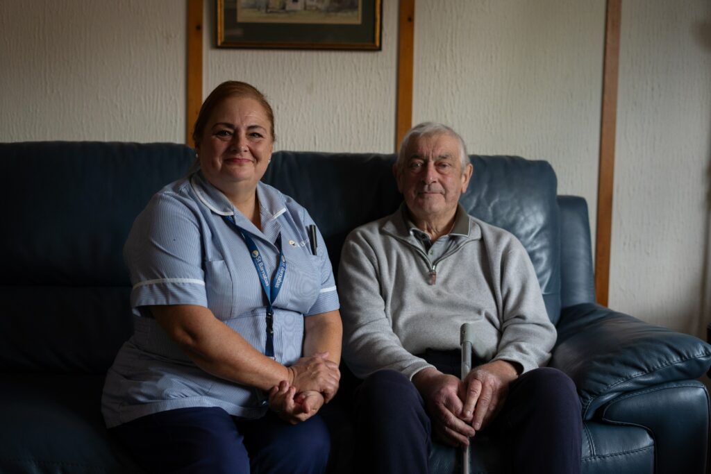 John sat on the sofa with Nurse, Julie, smiling at the camera.