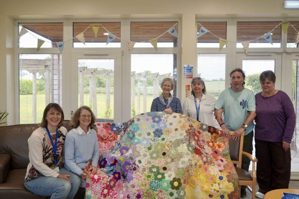 Members of the Louth creative wellbeing group, with Julia, stood next to the quilt and smiling at the camera