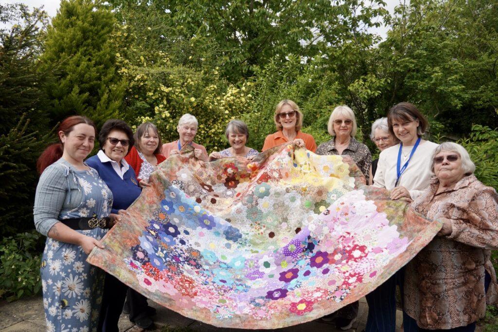 Members of the Lincoln creative wellbeing group holding the colourful quilt and smiling at the camera